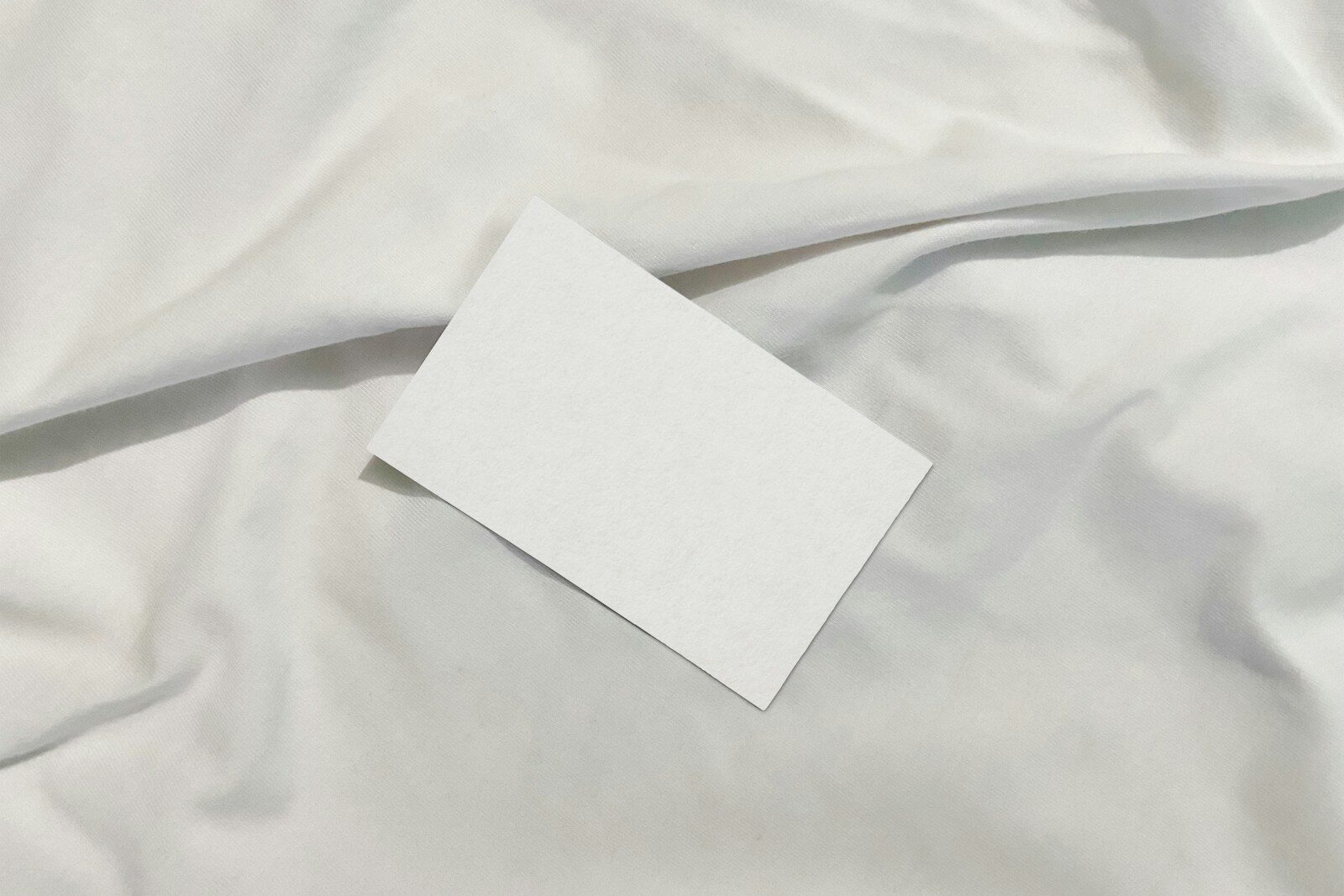 A blank white card rests on a wrinkled white fabric